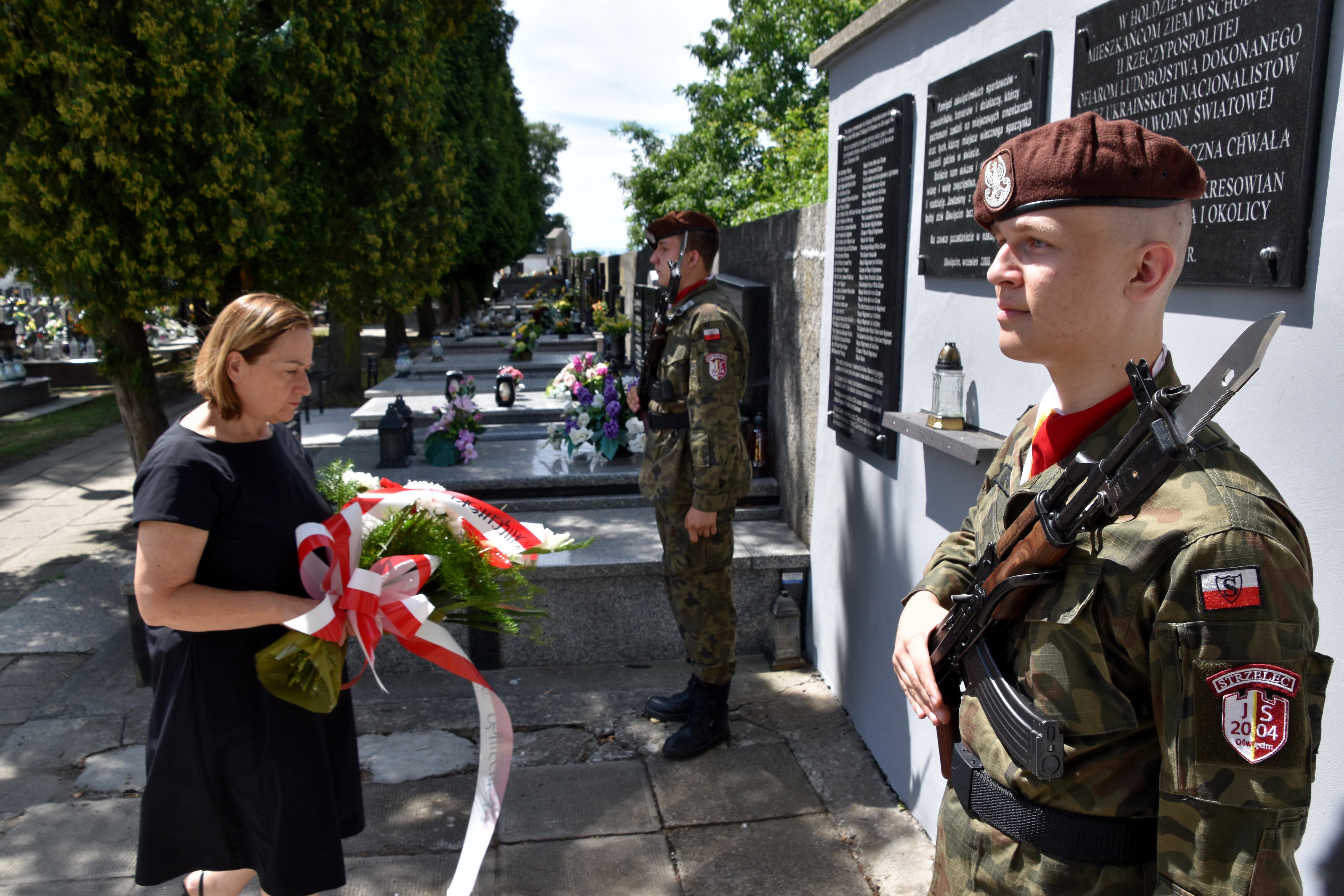 Wicestarosta Teresa Jankowska składa kwiaty pod tablicą pamiątkową na cmentarzu parafialnym w Oświęcimiu