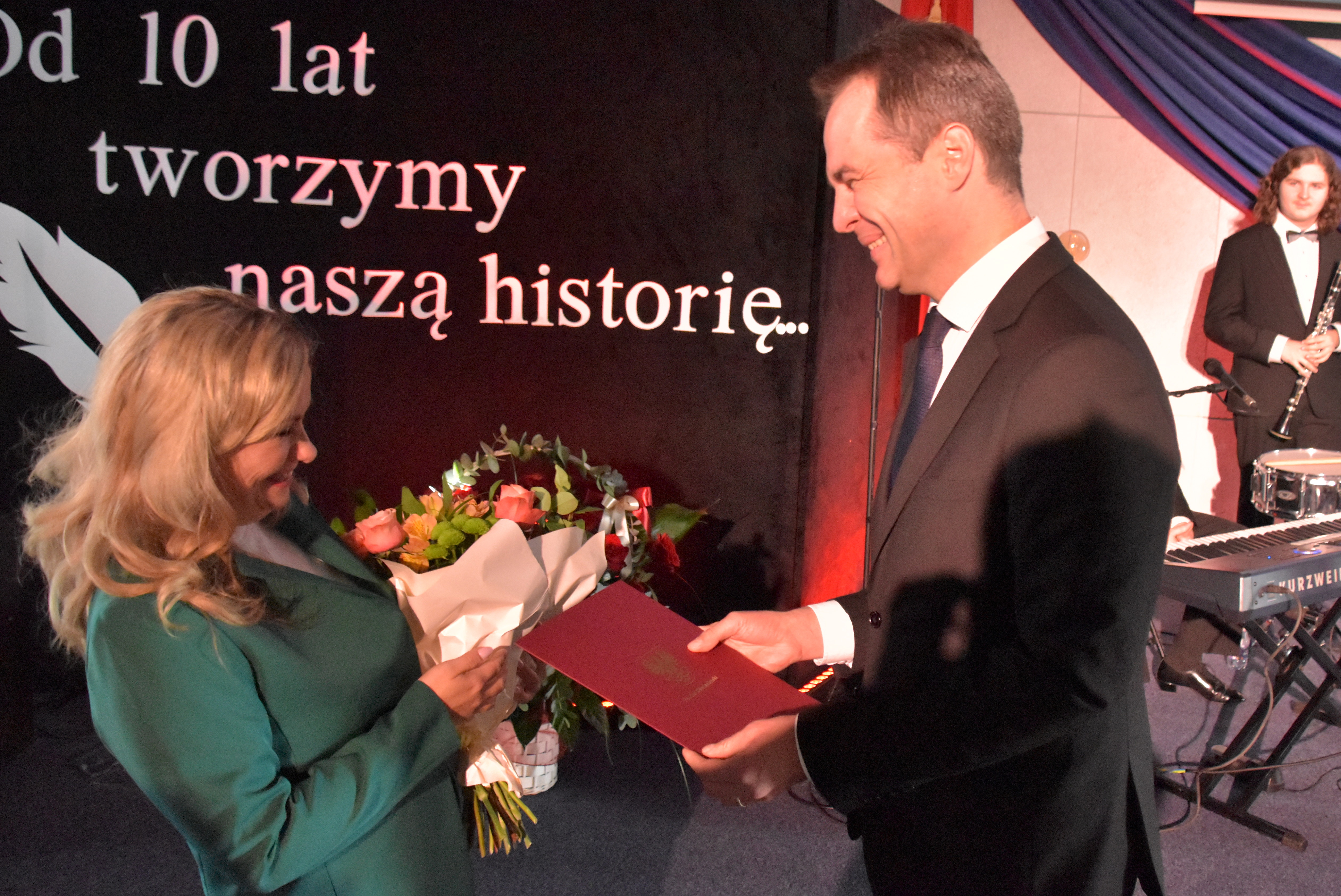 Starosta wręcza dyrektorce szkoły kwiaty i list gratulacyjny