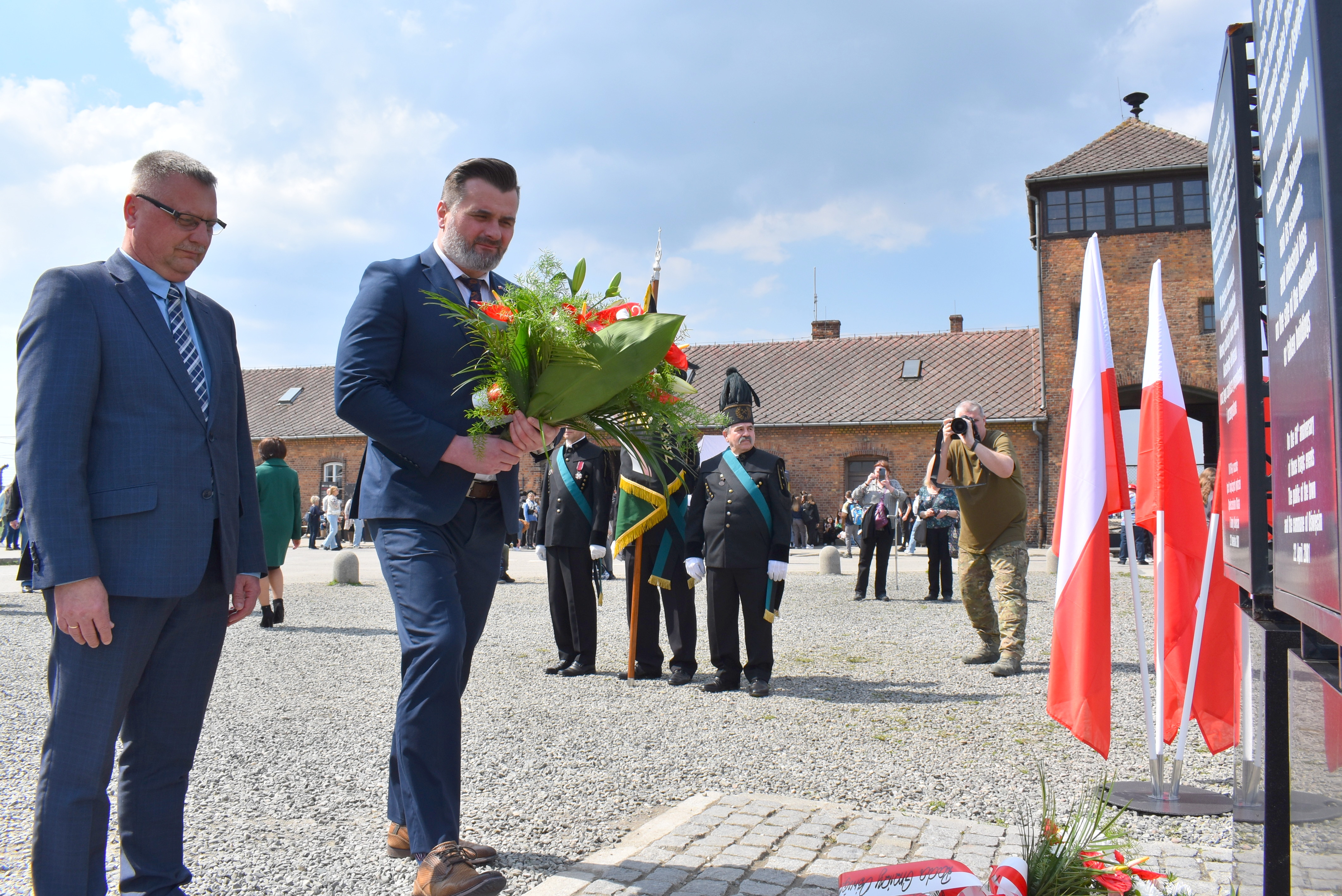 Na zdjęciu wicestarosta z wiązanką kwiatów i towarzyszący mu wiceprzewodniczący rady powiatu. W tle Brama Śmierci w byłym obozie zagłady Birkenau
