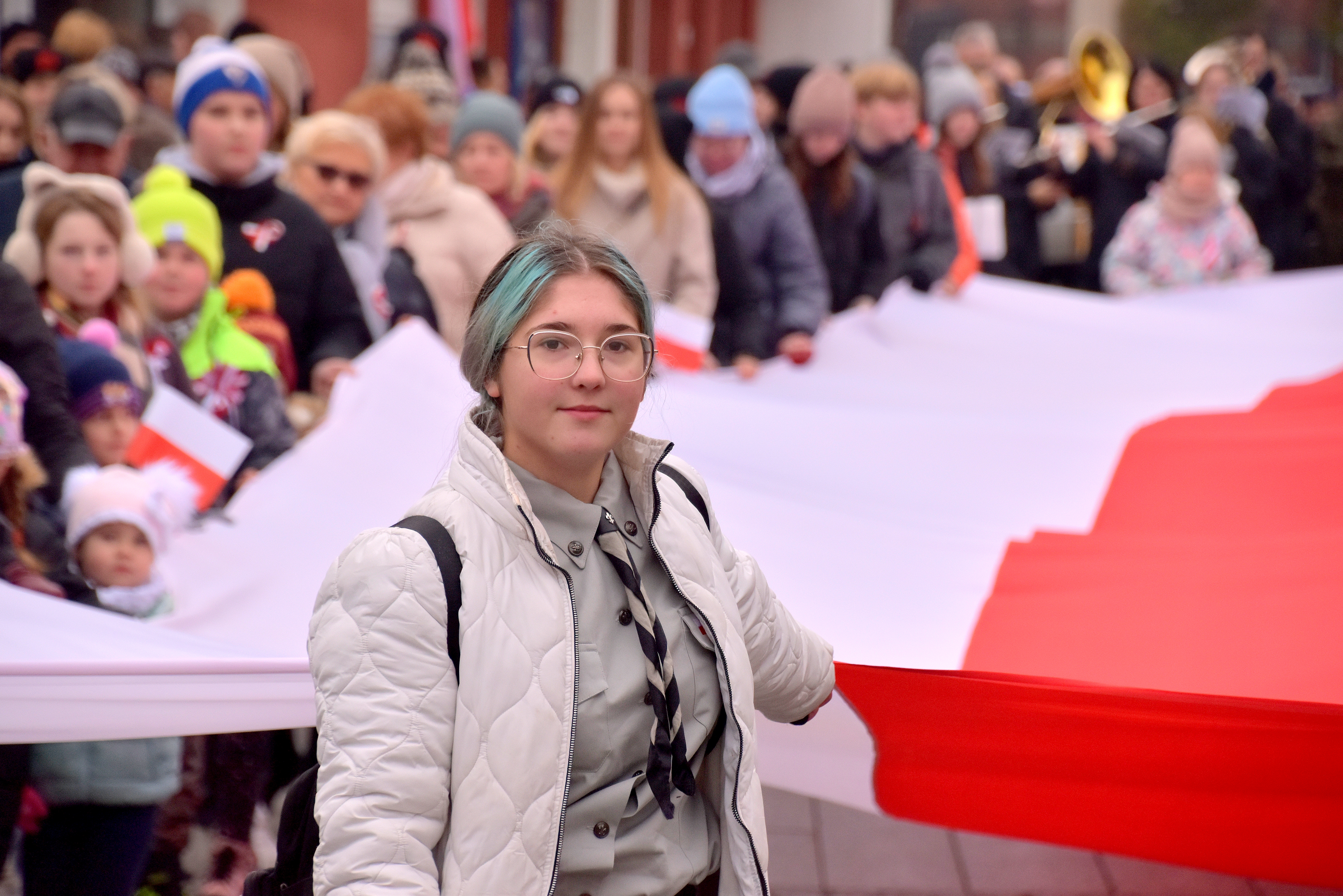 Harcerka na czele parady patriotycznej niosąca wraz z innymi wielką białą-czerwoną flagę