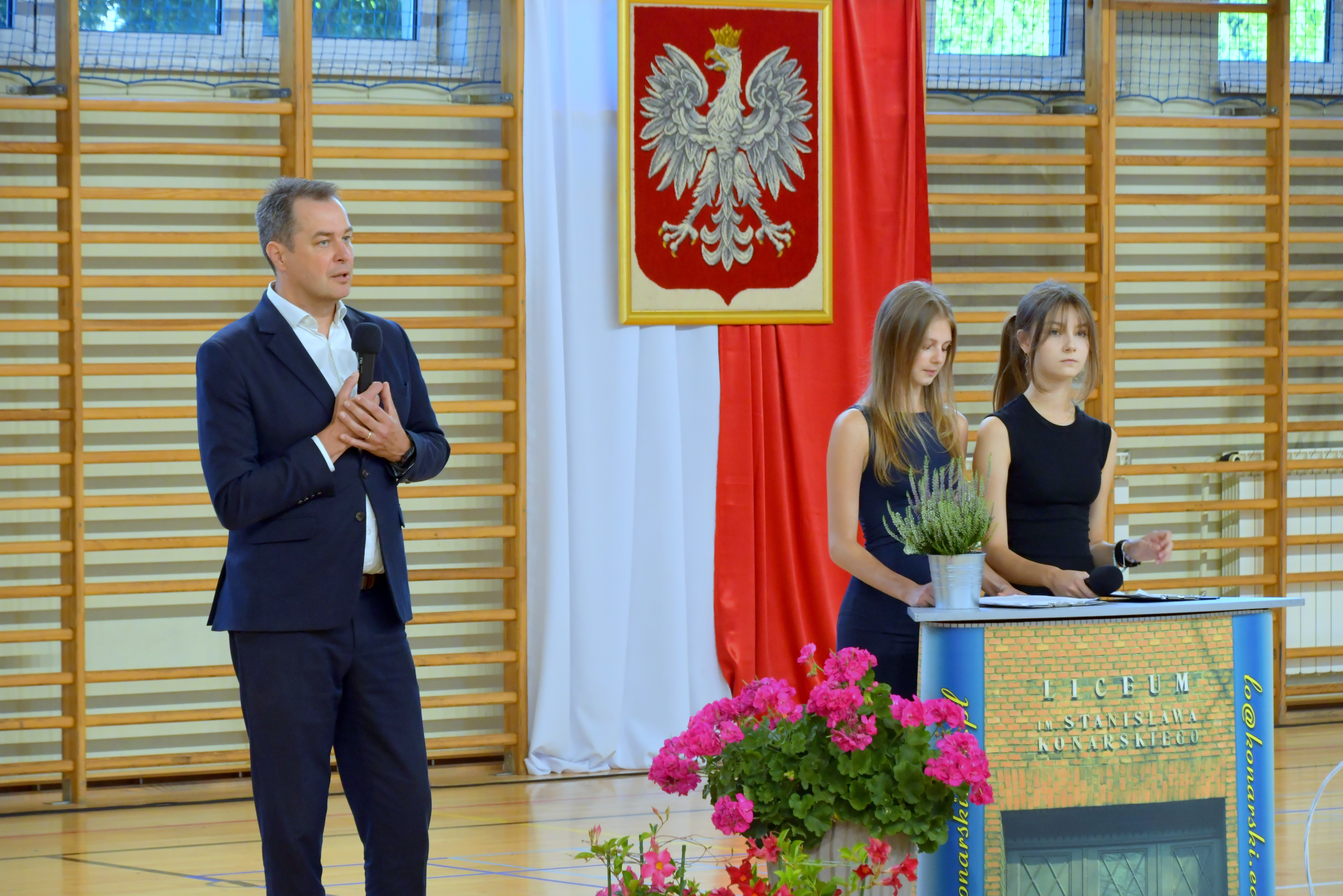 Starosta przemawia do uczniów liceum Konarskiego. Obok stoją dwie prowadzące spotkanie