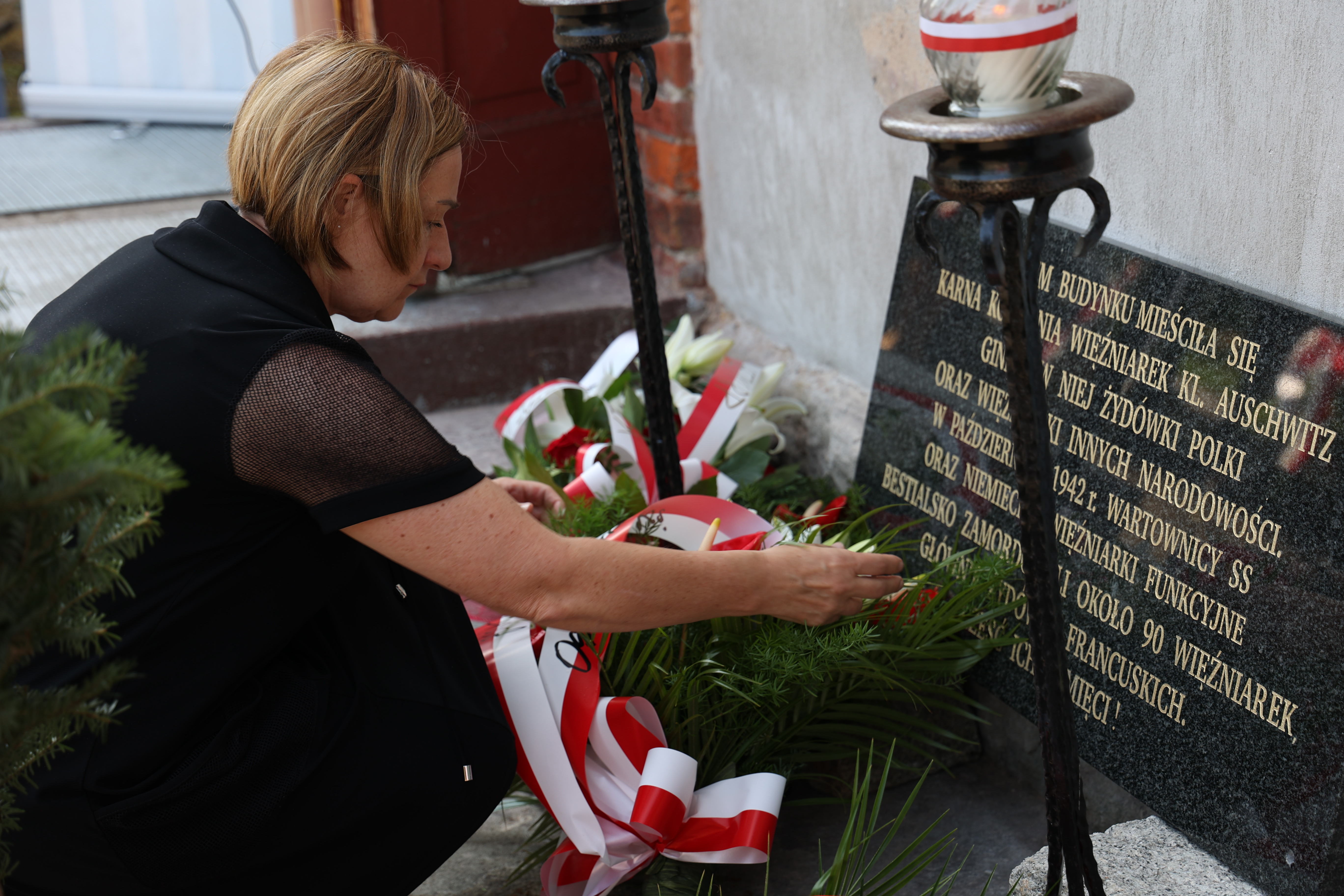 Teresa Jankowska składa wiązanki kwiatów przed tablicą upamiętniającą więźniarki karnej kompanii niemieckiego podobozu w Borze/Budach