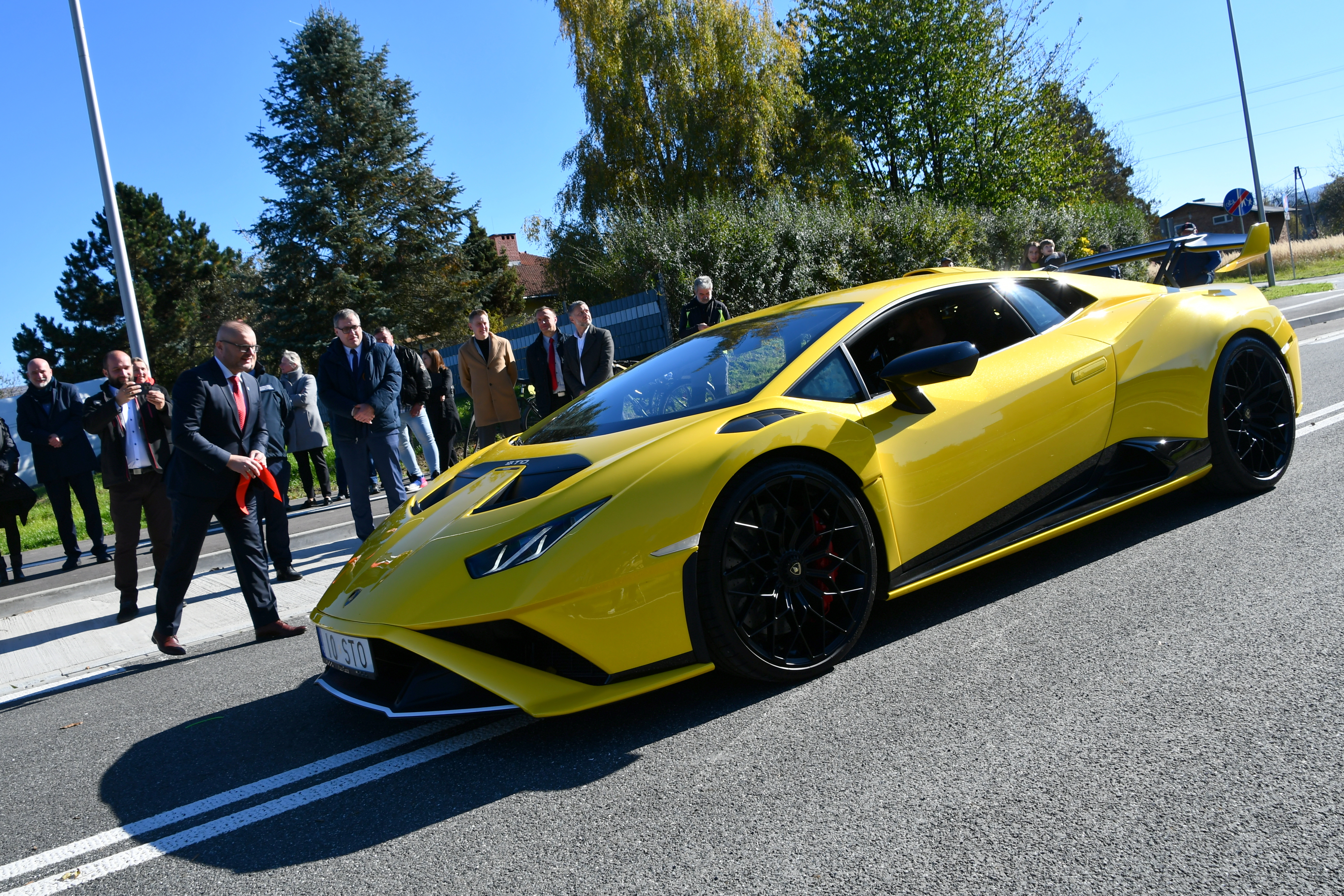 Burmistrz Kęt daje znak kierowcy żółtego lamborghini, by ruszył po nowym odcinku obwodnicy