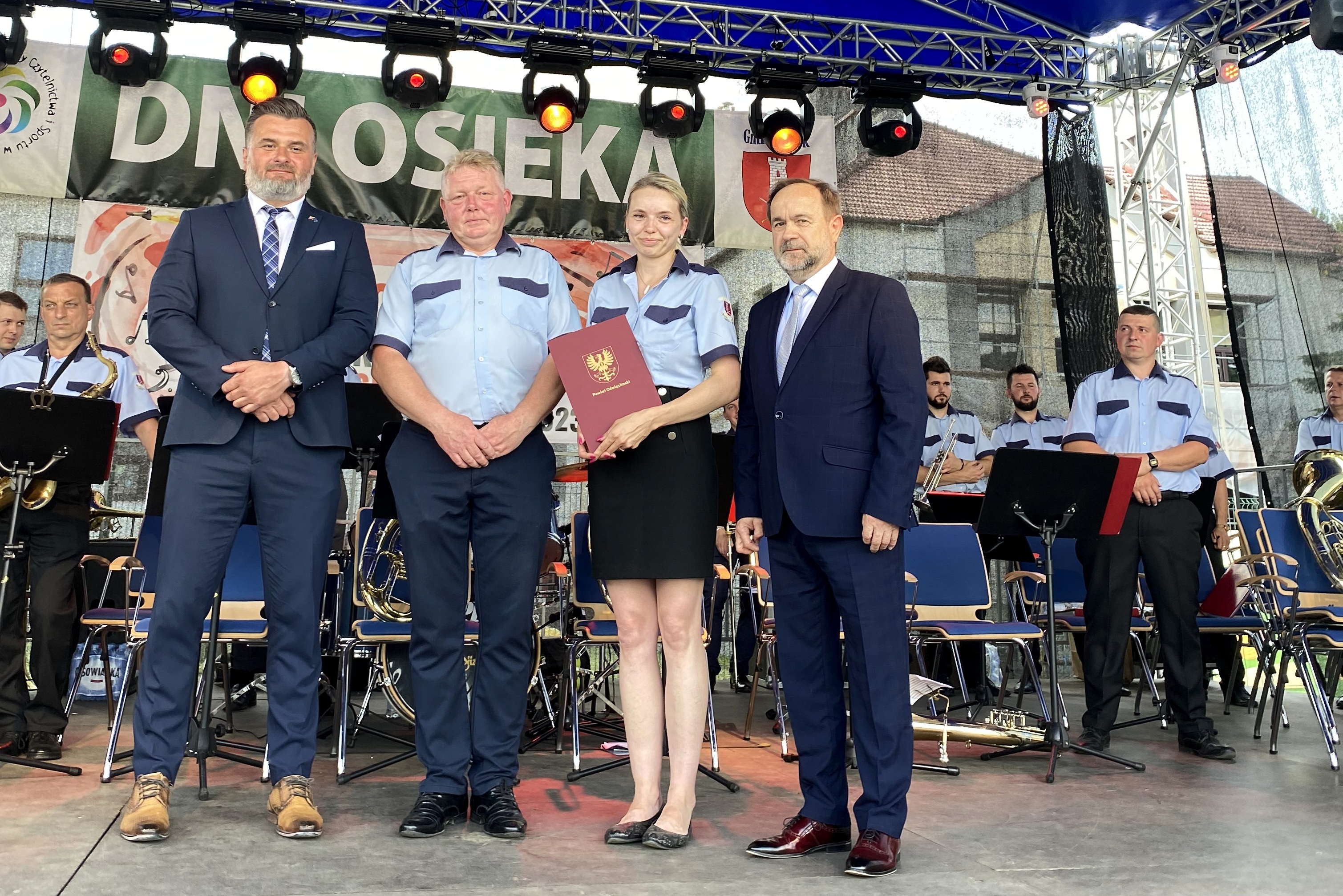 Na scenie stoją wicestarosta, członek zarządu oraz dwie osoby zawiadujące orkiestrą z Osieka