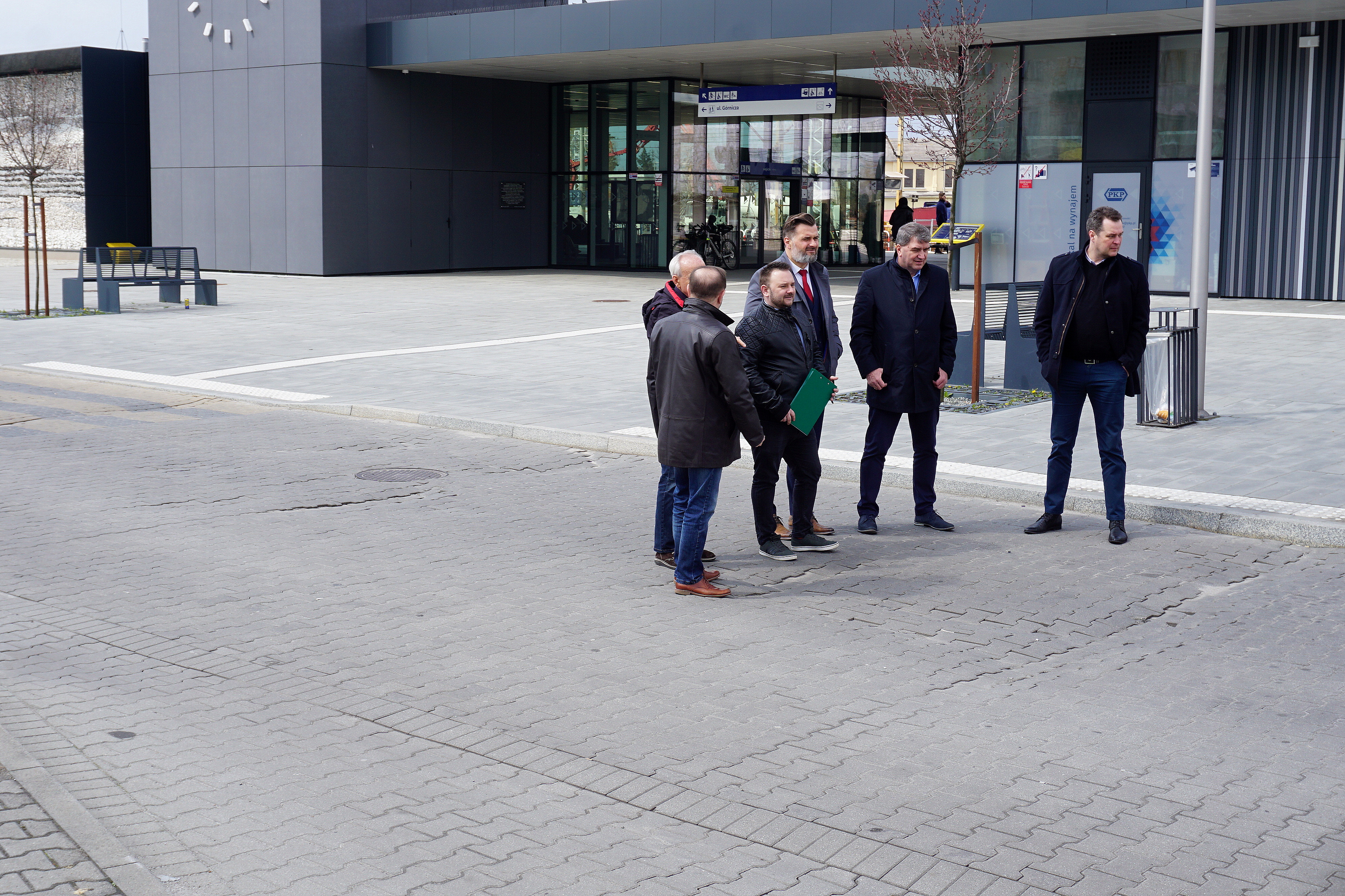 Na zniszczonej drodze przed dworcem kolejowym w Oświęcimiu stoją powiatowi i miejscy decydenci, w tym starosta Andrzej Skrzypiński i prezydent Janusz Chwierut.