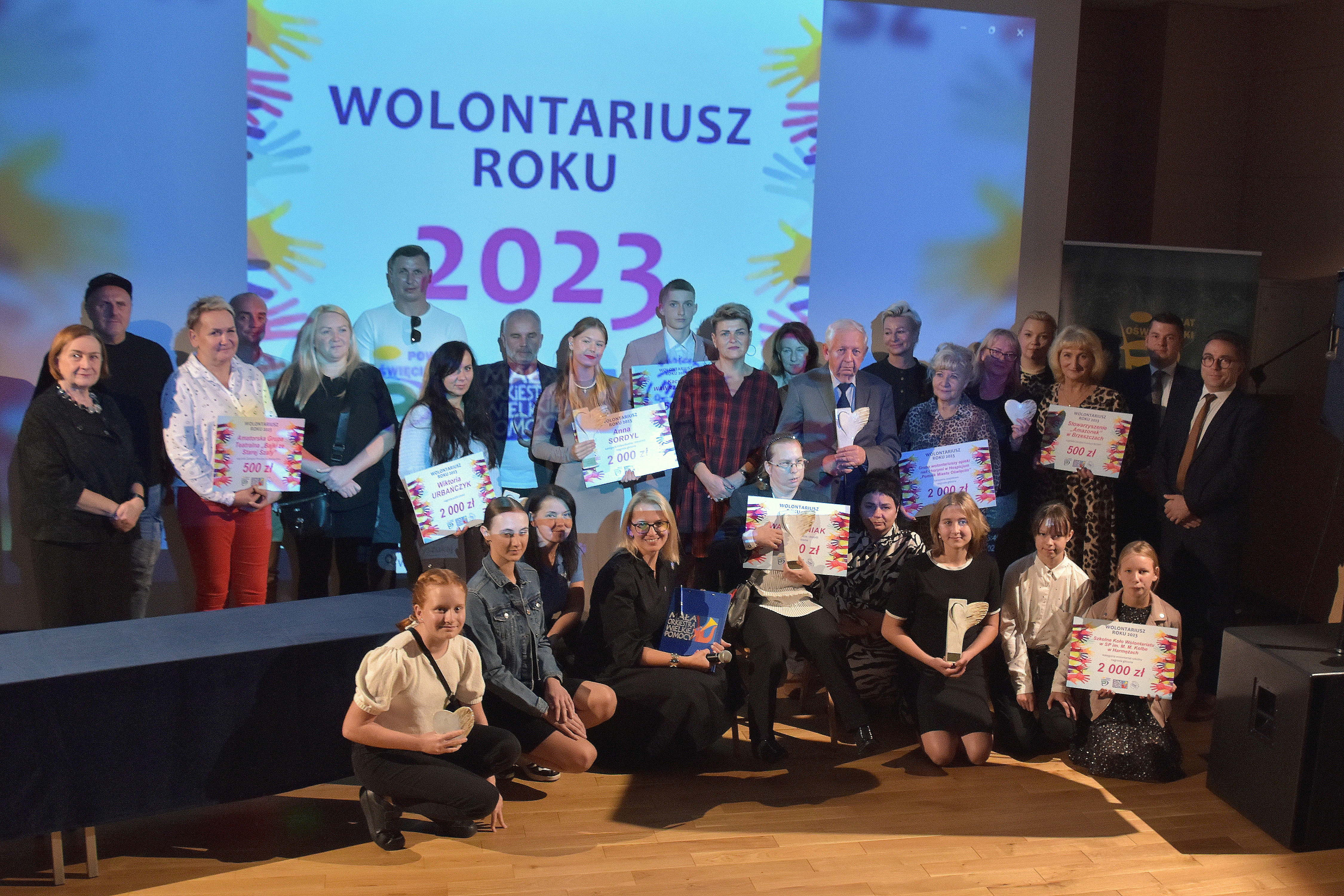 Pamiątkowe zdjęcie laureatów konkursu z organizatorami, w tle napis wolontariusz roku 2023