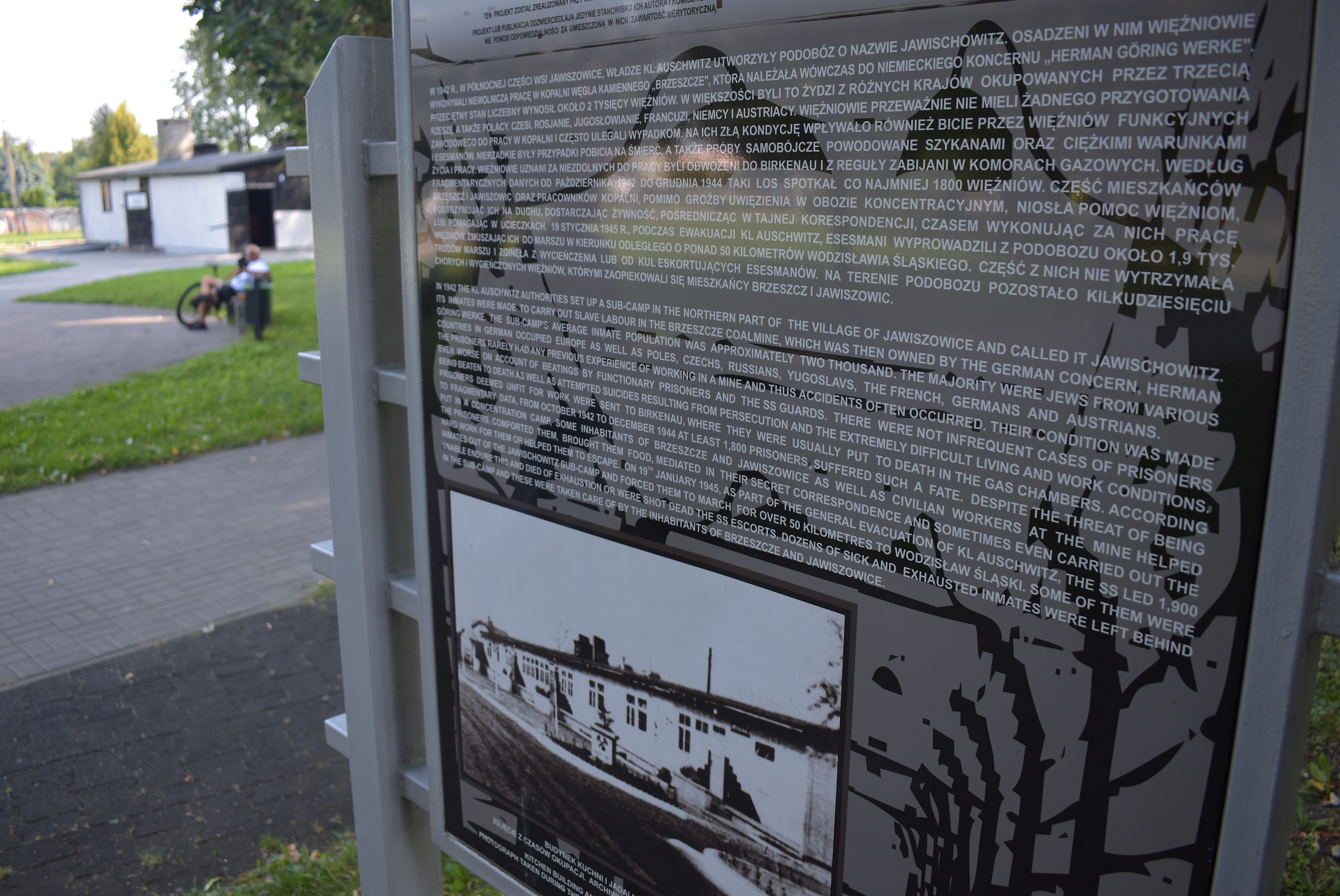 Tablica z informacją o historii podobozu, a w tle historyczna łaźnia obozowa