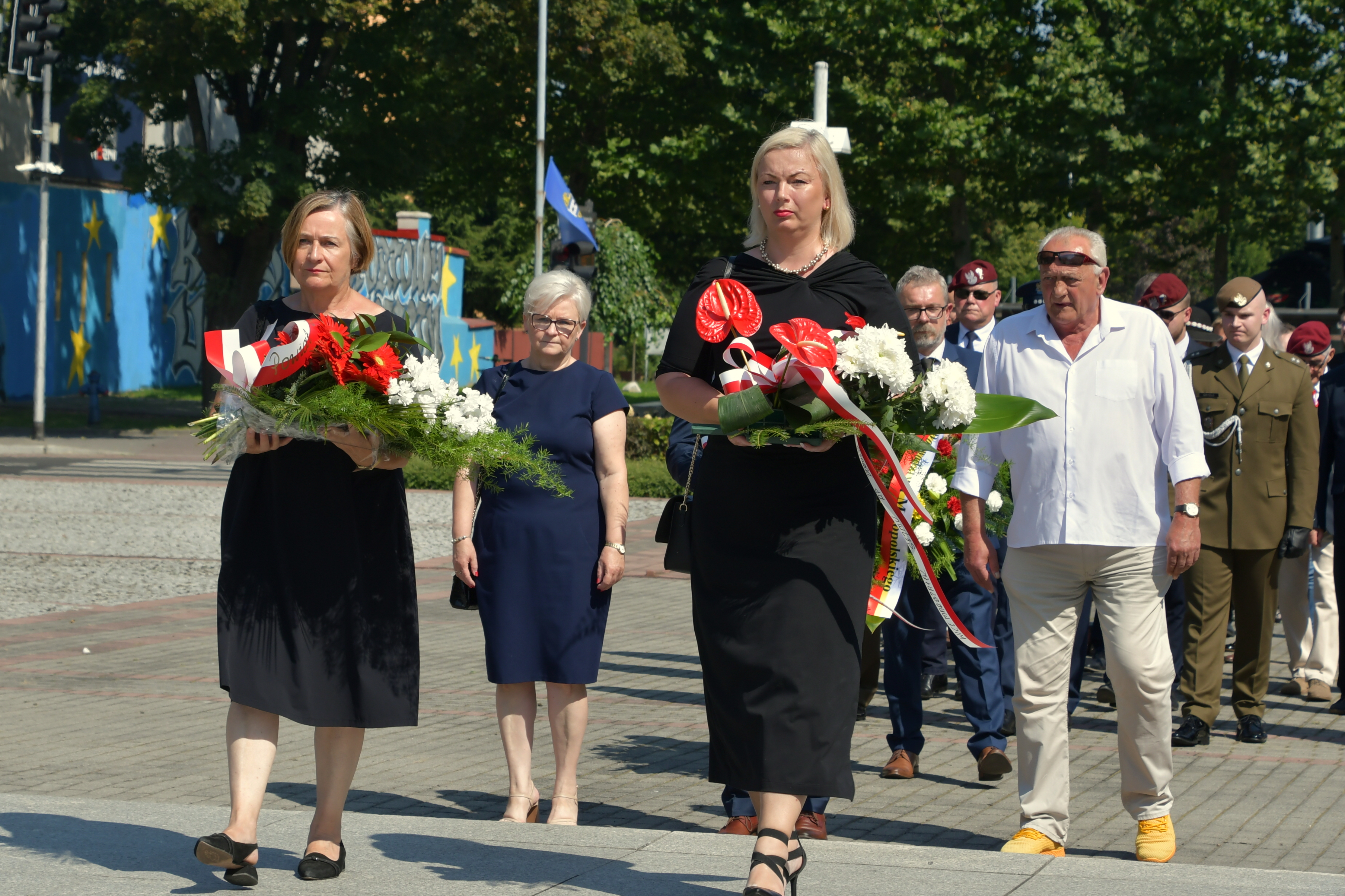 Wicestarosta i członkini zarządu powiatu z wiązankami kwiatów zmierzają w stronę Grobu Nieznanego Żołnierza