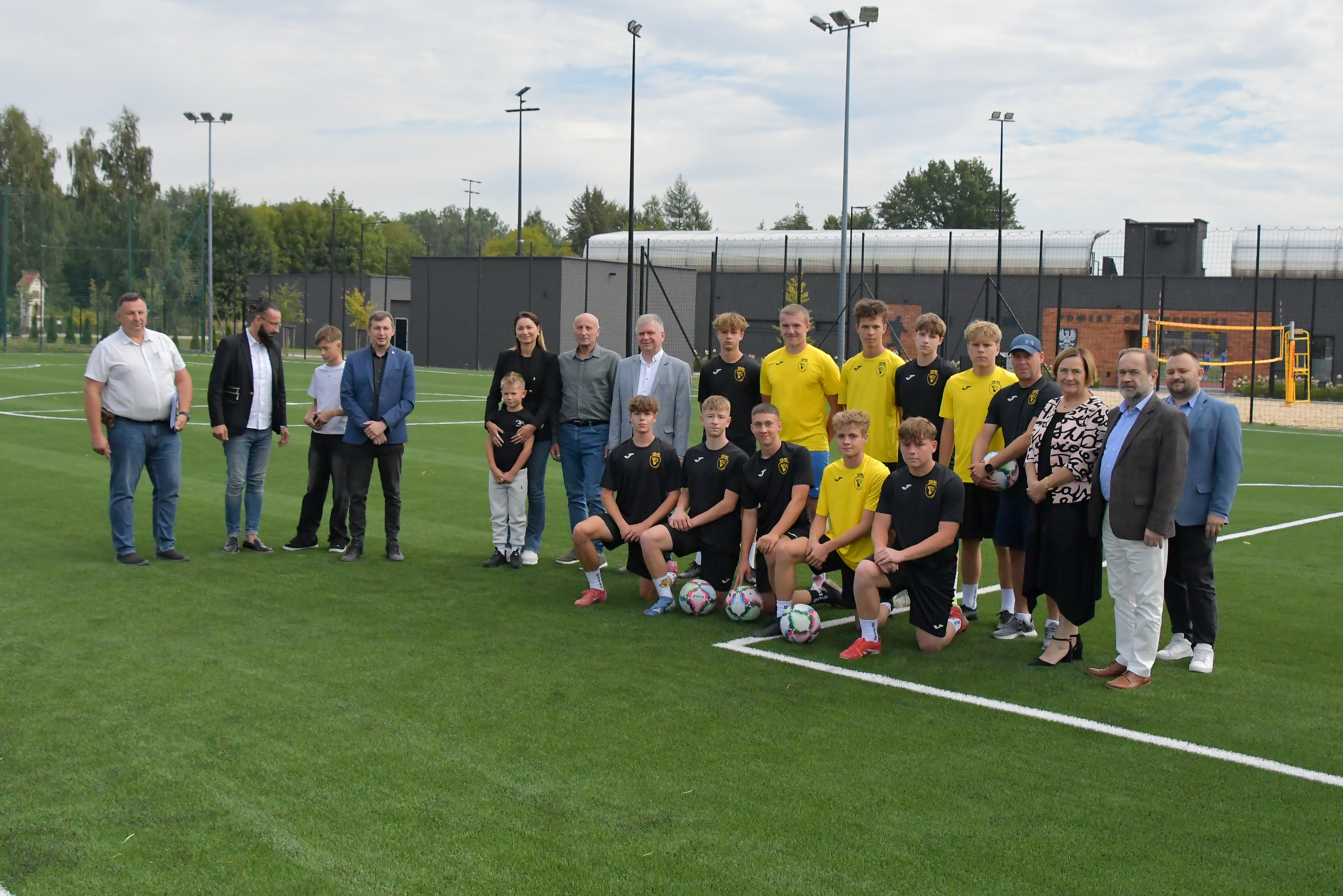 Pamiątkowe zdjęcie włodarzy, wykonawców zadania i sportowców na tle zmodernizowanego orlika
