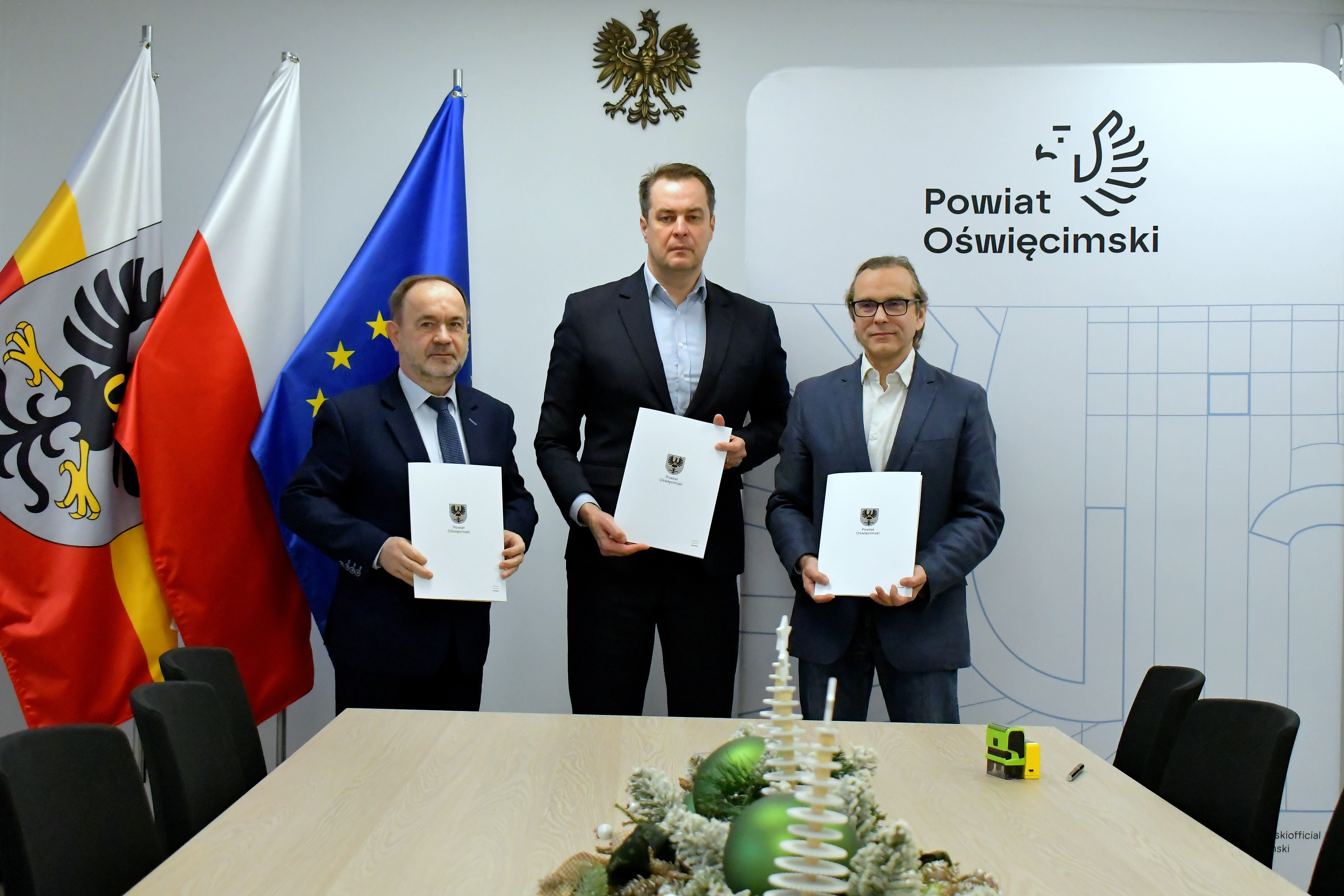 Pamiątkowe zdjęcie włodarzy Powiatu i przedstawiciela firmy na tle ścianki promocyjnej