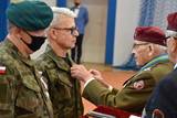 Osoba w mundurze po prawej stronie wręcza medal osobie po lewej stronie